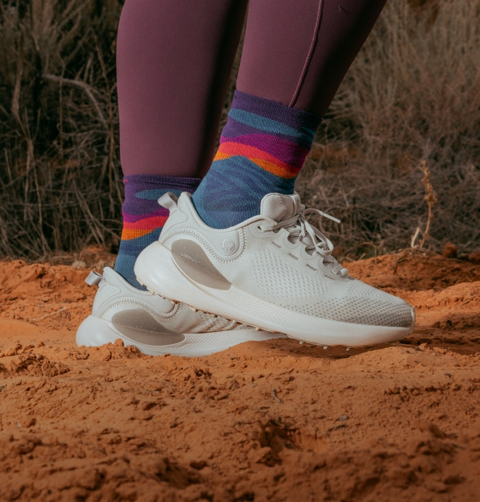 A pair of feet in Micro Crew height running socks with blue mountains and a sunset pattern